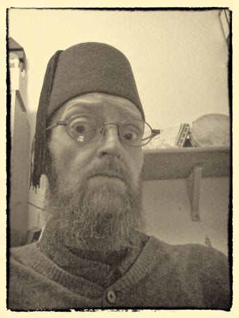 Sepia photo of Peet. Bearded man with glasses wearing a fez hat. Has a quizzical expression.